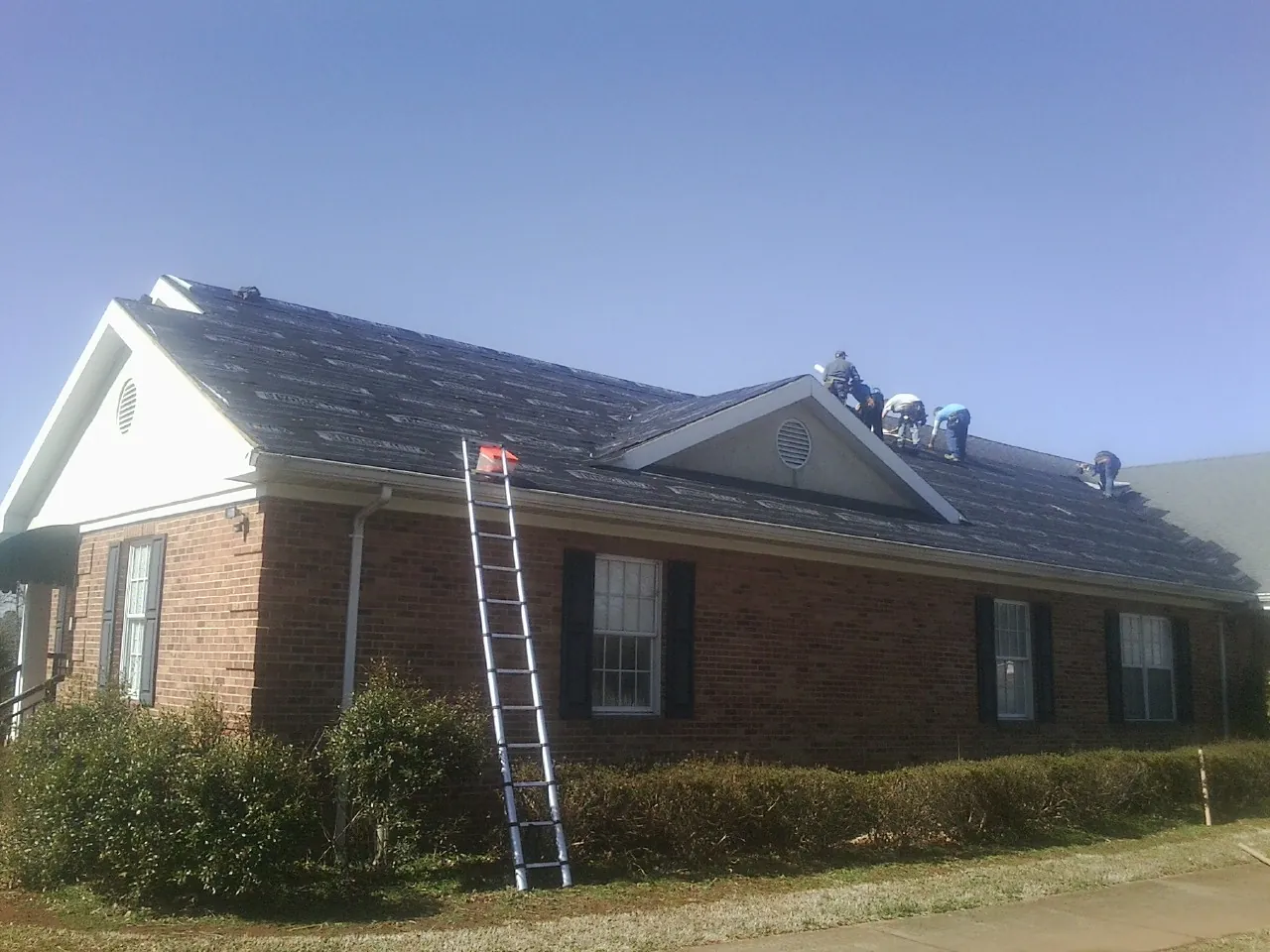 Crew tearing shingles off a brick ranch roof with a ladder set — Emergency Roof Repair work by our crew in Blenheim