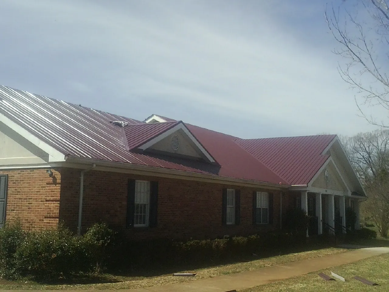 Red metal roof with gabled entries on a long brick building, from a Hail Damage Roof Repair job in Blenheim