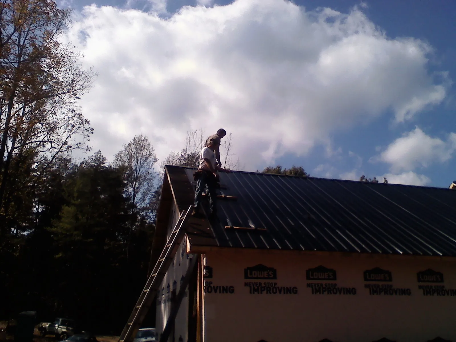 Roofer fastening dark metal panels high against a cloudy sky, from a Roof Inspection job in Blenheim
