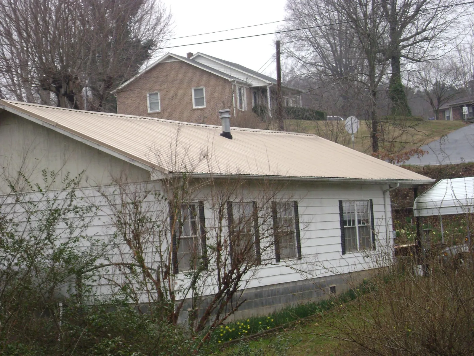 Tan metal roof on a white sided house set into a hillside — Commercial Roofing by Roofing Brothers in Blenheim